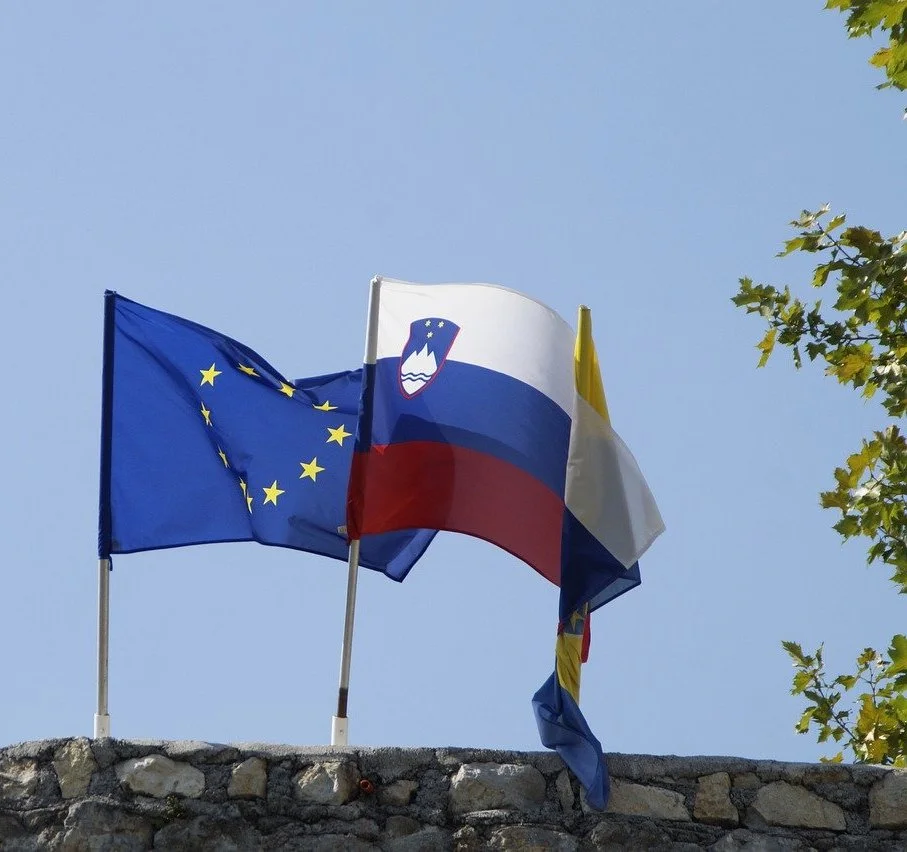 Flags of Slovenia, the European Union, and Russia displayed together on flagpoles.