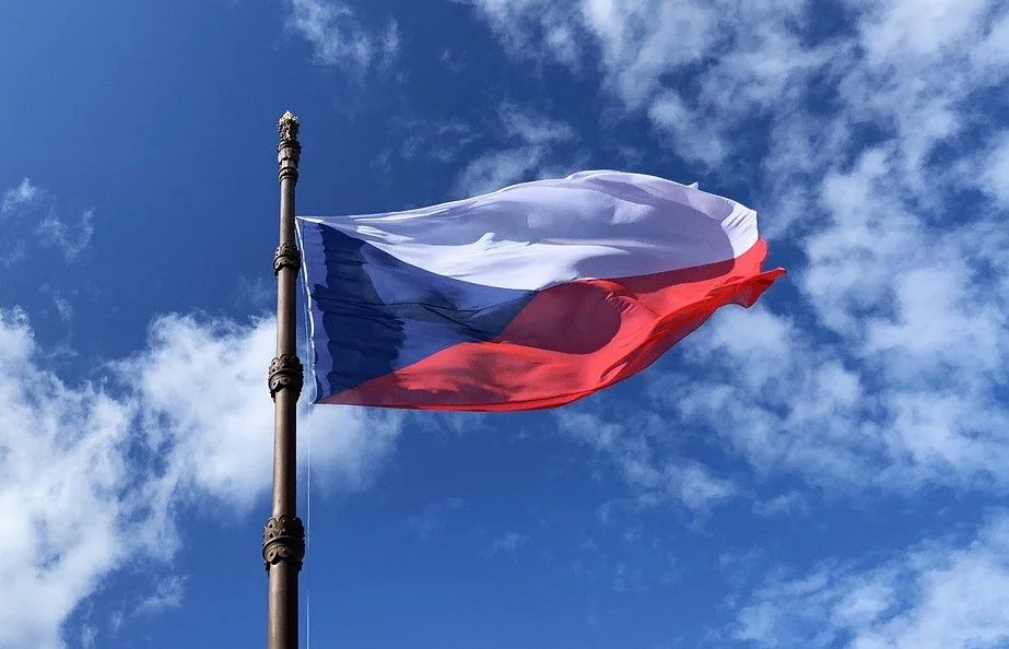 Czech Republic flag waving on a flagpole against a blue sky with clouds.